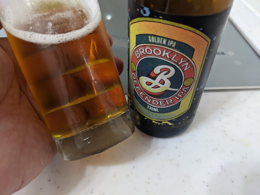 「ブルックリンディフェンダーIPA」が入ったグラスを斜め左に傾けているところ