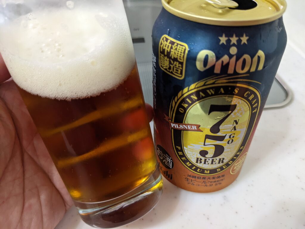「75（名護）ビールピスルナー」が入ったグラスを傾けているところ